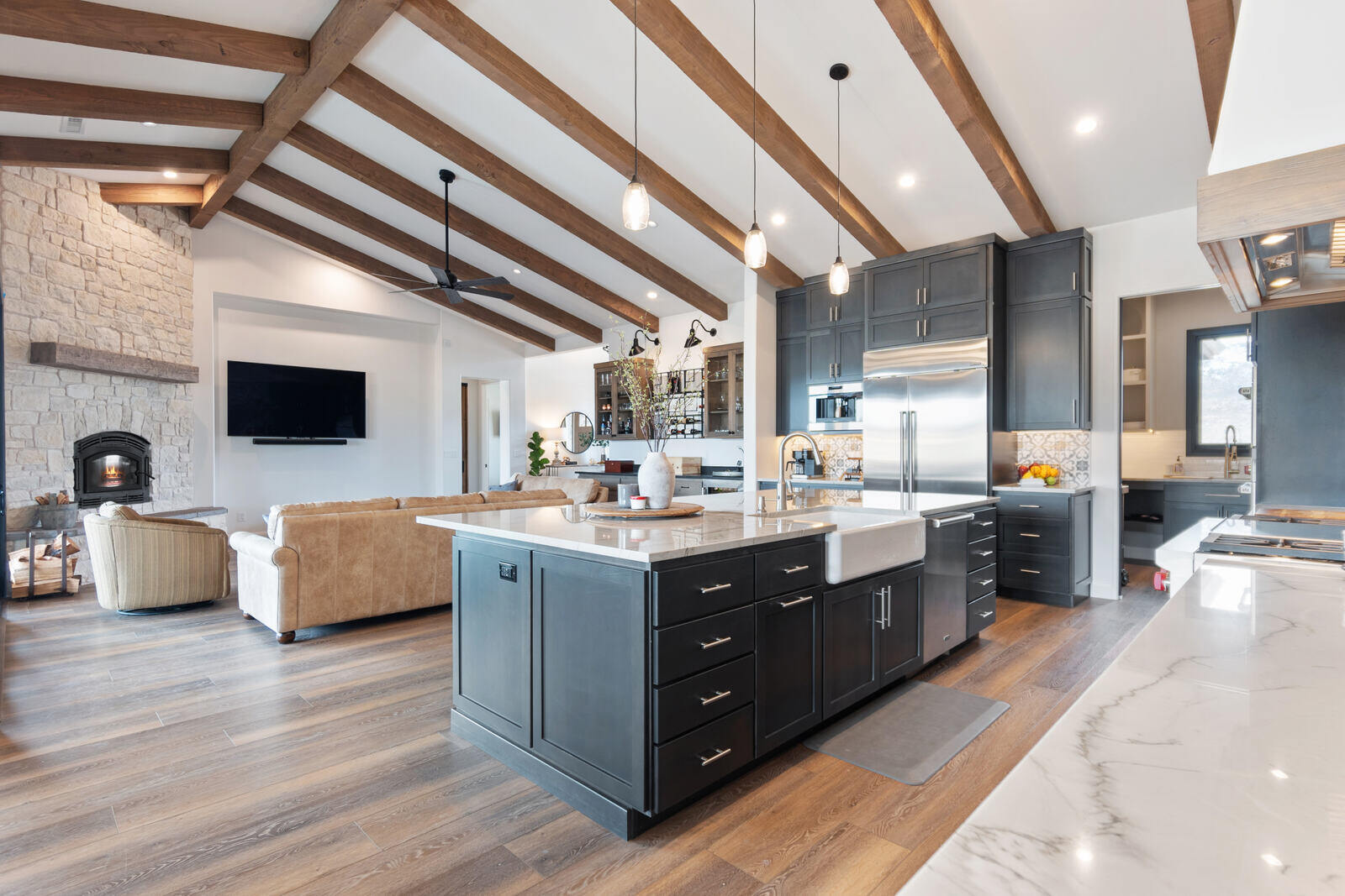 Open-concept kitchen and living area in a whole home remodel by Triple Crown Contractors in Raleigh, NC, featuring exposed wood beams, a large island, and a stone fireplace